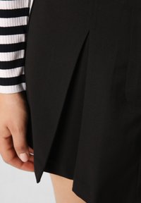 Zwarte geplooide rok met een gladde textuur en zijnaadzakken, gecombineerd met een lang mouw wit en marineblauw gestreept bovenstuk.