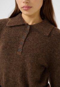 Braunes Wollmischgewebe-Oberteil mit Kragen, fünf schwarzen Knöpfen und einer weichen, flauschigen Textur. Nahaufnahme, die die feinen Fasern zeigt.