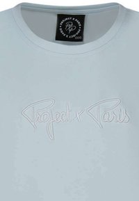 T-shirt bleu clair avec un col rond et un logo brodé blanc "Project x Paris" à l'avant. Texture de tissu lisse.