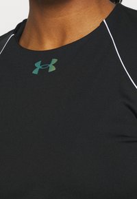 Musta urheilupaita, joka on valmistettu sileästä ja joustavasta materiaalista. Kyljessä on vihreä Under Armour -logo ja valkoista ompelua kaula-aukolla.