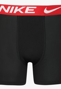 Črne bokserice iz gladkega materiala z rdečim elastičnim pasom, ki nosi Nike logo v belem.