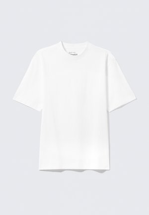 Camiseta blanca lisa de manga corta con corte holgado y cuello redondo, mostrada sobre un fondo plano de color gris claro.