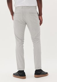 Pantalones gris claro con una tela texturizada, corte ajustado, dos bolsillos traseros con botones y puños enrollados, combinados con zapatillas negras.