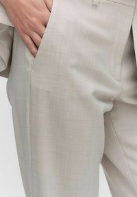 Beige-harmaat tailored-housut, joissa on hienostunut teksturoitu kuvio, yhdellä sivutaskulla ja suoran istuvuuden muotoilulla. Silkkisen sileä kangaspinta.