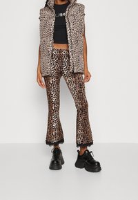 Puffervest im Leopardenmuster und passende ausgestellte Hose, mit schwarzen Spitzenakzenten, kombiniert mit klobigen schwarzen Plateau-Schuhen.