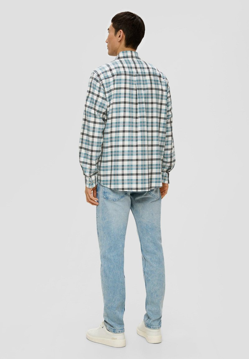 Chemise à manches longues à carreaux en blanc, bleu et noir ; elle présente un col boutonné et un ourlet droit. Portée avec un jean bleu clair et des chaussures blanches.