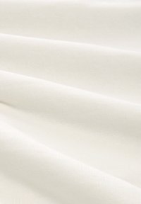 Tissu en coton de teinte ivoire douce, présentant une texture côtelée subtile et une surface lisse, drapé pour montrer son fluidité et sa structure.
