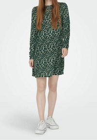 Vestido de manga larga en verde oscuro con estampado de leopardo, fabricado en tejido suave, con un corte holgado, y combinado con zapatillas blancas.
