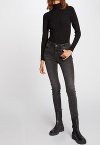Suéter negro de cuello alto con canalé texturizado, combinado con jeans ajustados de tiro alto en gris oscuro y botas de tobillo negras gruesas.