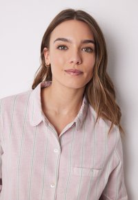 Camicia button-up rosa chiaro con righe verticali bianche e verdi, colletto e taschino sul petto con un dettaglio a bottone singolo.