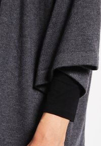 Arm wearing a black long-sleeve shirt under a loose, dark gray knit sweater sleeve.
