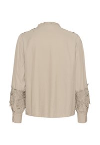 Blouse beige clair avec des manches longues et volumineuses. Présente une bordure en dentelle texturée aux poignets et un col froncé pour un détail supplémentaire.