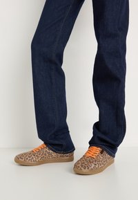 Baskets en toile à imprimé léopard avec lacets orange, semelles en caoutchouc, associées à un jean en denim bleu foncé à coupe droite.