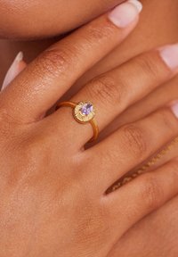 Gold ring with textured band, featuring a central oval amethyst gemstone, set in a sunburst pattern. Smooth and polished finish.