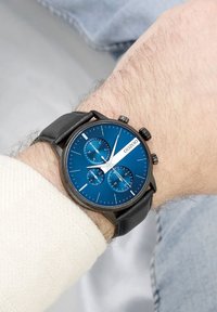 Montre chronographe avec un cadran bleu, un boîtier noir et un bracelet en cuir. Présente trois sous-cadrans, des accents argentés et des index horaires blancs.