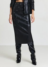 Gonna midi in pelle nera decorata con borchie argentate, design slim fit, trama liscia, abbinata a stivali neri lucidi al ginocchio.