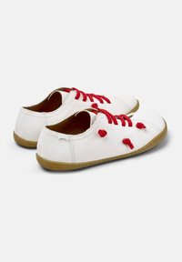 Chaussures en cuir blanc avec des lacets et des accents rouges, présentant un bout rond et une semelle en caoutchouc beige, mettant en avant un design minimaliste.