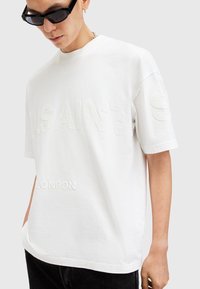 White cotton t-shirt with raised text "SAINTS" and "LONDON" in light embroidery, featuring short sleeves and a relaxed fit.