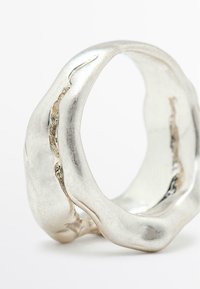 Anello in argento texturizzato con un design ondulato, caratterizzato da una finitura lucida e da una cucitura verticale. Forma arrotondata, bordi lisci e ampiezza consistente.