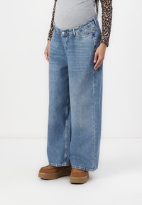 Wide-leg blue denim jeans with a faded finish, featuring a standard waistband and five-pocket design, worn with brown platform shoes.