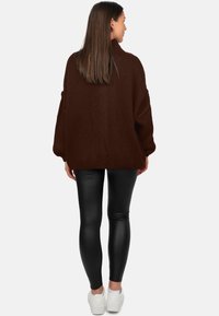 Pull en maille marron oversize avec un col haut, associé à des leggings noirs et des baskets blanches. La texture semble douce et épaisse.