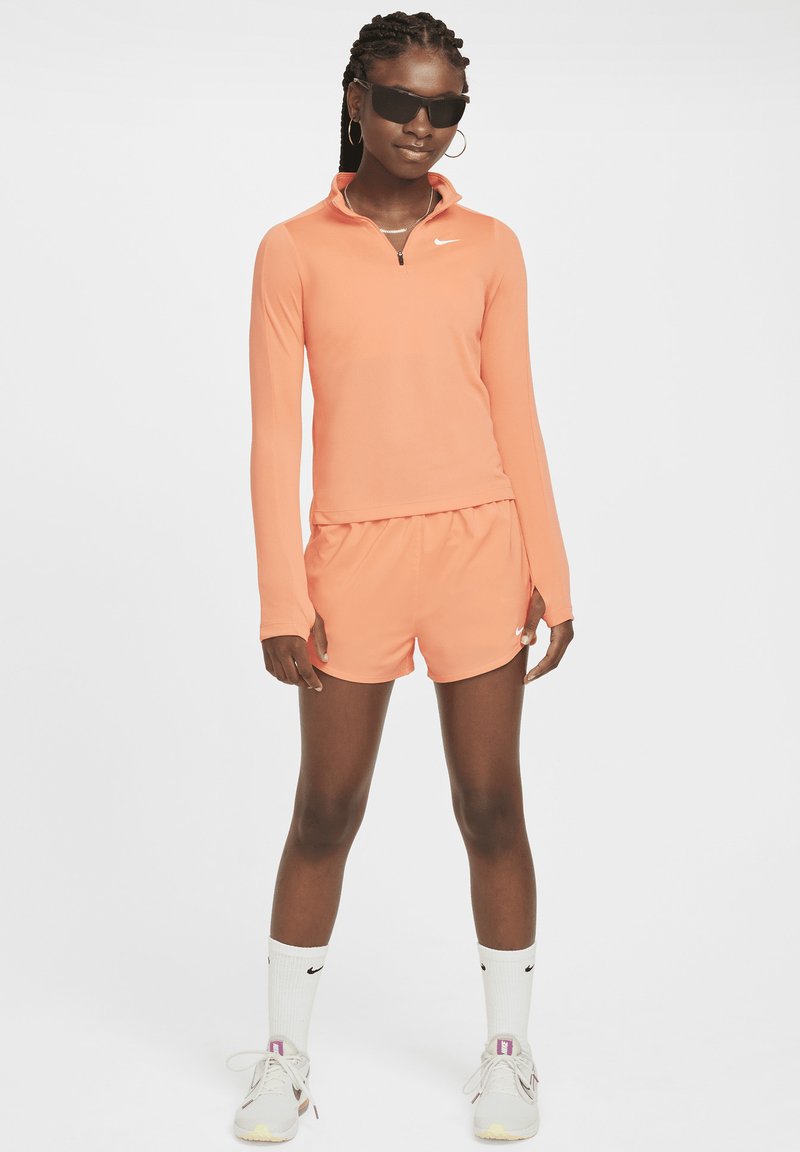 Oranges langärmliges Sportoberteil mit Viertelreißverschluss und passenden Shorts. Tragen mit Sonnenbrille und Sportsocken, dazu helle Schuhe.