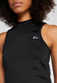 Haut noir sans manches avec un col montant et une coupe ajustée. Présente un petit logo blanc sur le haut du côté gauche. Tissu lisse et extensible.