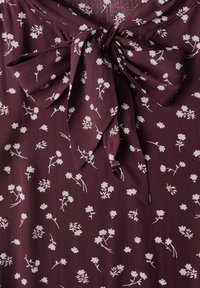 Tissu violet foncé avec un petit motif floral blanc, noué en un grand nœud au centre.