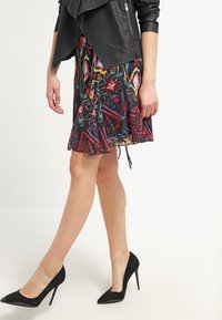 Giacca di pelle nera sopra una gonna multicolore con un motivo floreale e geometrico. Tacchi a spillo neri completano il look.
