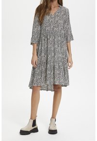 Šaty s potiskem zvířecí kůže v černobílé barvě, s výstřihem do V, volánkovou sukní a rukávy do tří čtvrtin, doplněné béžovými kotníkovými botami s černou podrážkou.