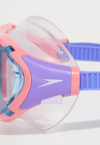 Roze en paarse zwembril met heldere lenzen, voorzien van een flexibele behuizing, gestructureerde bandjes en een herkenbaar logo aan de zijkant.