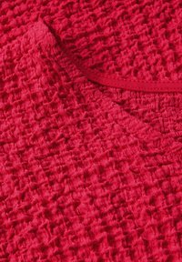 Tejido rojo texturizado con un patrón arrugado; presenta un escote suave y un color rico y vibrante. Parece ligero y transpirable.