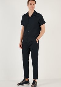 Zwarte korte mouwen shirt met verticale strepen, knoopsluiting ontwerp; gecombineerd met zwarte tapered broek en zwarte sneakers met grijze accenten.