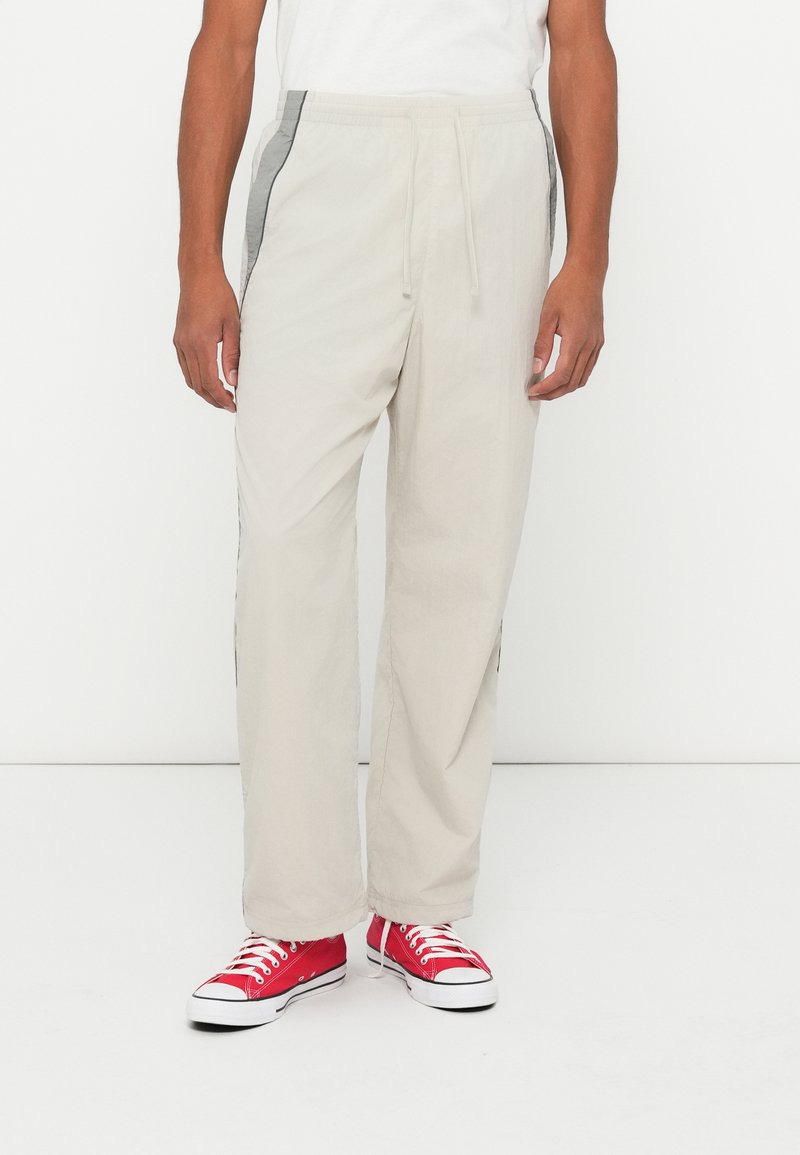 Jasnobeżowe spodnie o luźnym kroju z szarymi bocznymi panelami. Wykonane z lekkiego materiału, z elastycznym pasem. Połącz z czerwonymi sneakersami.