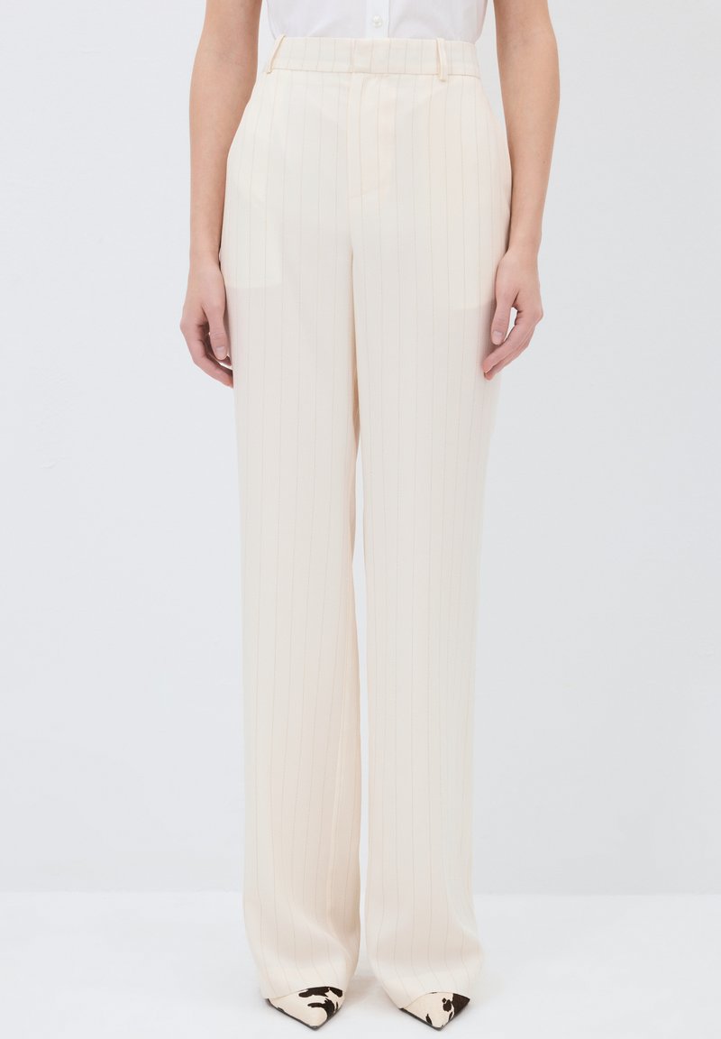Pantalon large beige avec des rayures verticales, fabriqué en tissu léger. Il présente une taille haute et un devant plat avec des poches latérales.