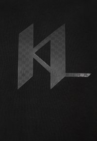 Tela negra con un logo gris texturizado en forma de "K" y "L" angulares, con un patrón en relieve para mayor detalle.