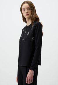 Maglietta nera a maniche lunghe con scollo tondo e un design arricchito di accenti e motivi argentati sul davanti. Tessuto dalla texture liscia.