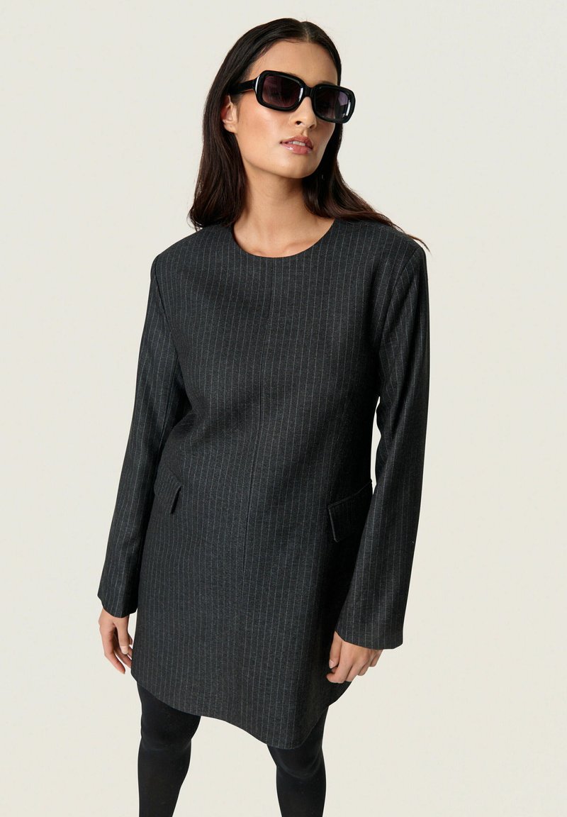 Schwarzes Kleid mit Nadelstreifen, rundem Ausschnitt, langen Ärmeln und seitlichen Taschen. Aus einem strukturierten Stoff gefertigt, knielang.