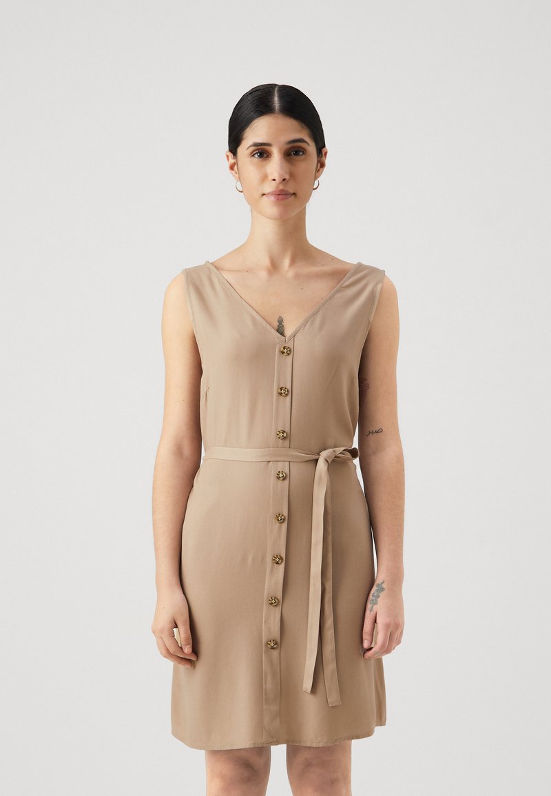 Beige ermeløs kjole med V-hals, frontlukking med knapper og belte i midjen. Glatt stoff og knelengde. Subtil glans.