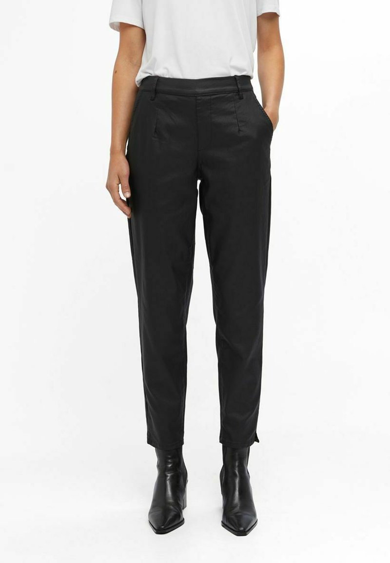 Pantalons noirs fuselés avec une finition en tissu lisse, dotés de poches latérales et d'une taille plate, accompagnés de bottines noires à bout pointu.