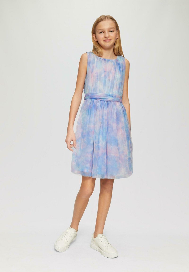 Ein ärmelloses Kleid in Pastellblau und -rosa Farben, mit einem plissierten Design und einem Stoffgürtel in der Taille, kombiniert mit weißen Sneakers.