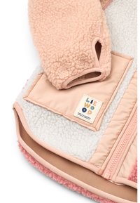 Ζακέτα από φλις με απαλό ροζ εξωτερικό, εκρού εσωτερικό και μπεζ φερμουάρ. Περιλαμβάνει ετικέτα με λογότυπο και στρογγυλή τσέπη για ευκολία.