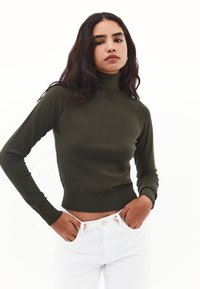 Olijfgroene coltrui met een strakke pasvorm, ribbelmanchetten en zoom, gecombineerd met witte broek, wat zorgt voor een gestroomlijnd silhouet.