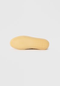 Semelle en caoutchouc avec une texture lisse et jaune ; présente une forme courbée et une surface de préhension à motifs pour une bonne adhérence.