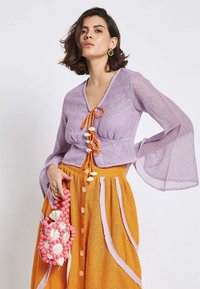 Lavender sheer knit top with orange drawstring and shell details; paired with an orange textured skirt featuring pink stripes and buttons.
