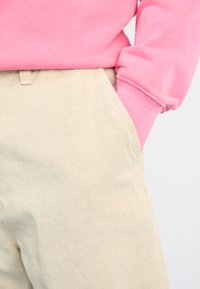 Rosa Sweatshirt mit gerippten Bündchen, kombiniert mit hellbeigen Hosen mit Seitentaschen und einer strukturierten Oberfläche.
