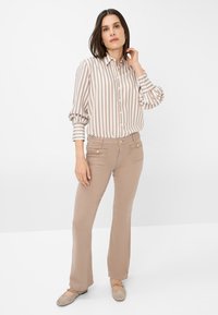 Gestreifte Bluse in Beige und Weiß, lässige Passform, mit Knöpfen. Kombiniert mit hellbraunen, ausgestellten Hosen mit Fronttaschen und goldenen Akzenten.