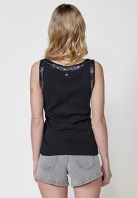 Must have mustaravärvi tank top, millel on tekstuuriga pind, kaunistatud läikiva perlekrae äärega. Ühendatud hallide teksashortsidega, näidates sooja ja mugavat stiili.