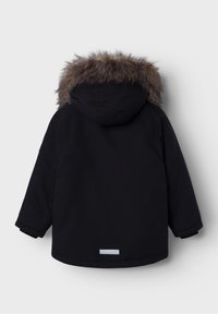 Parka noire avec capuche bordée de fourrure, au design simple, coupe légèrement oversized, et bande réfléchissante à l'ourlet. Texture douce.