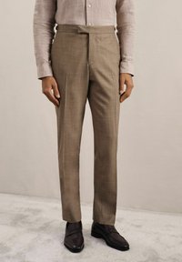 Pantalons beige ajustés avec un design à plat, fabriqués à partir d'un tissu texturé. Caractéristiques d'une taille haute et portés avec des mocassins foncés.